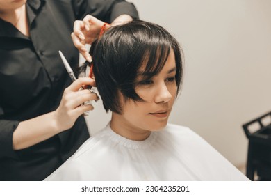 hairdresser makes a haircut to a woman in the salon. The hairdresser cuts wet hair, combing with a comb. client with short hair. back view - Powered by Shutterstock