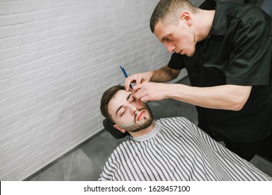 Hairdresser makes a stylish men's hairstyle with a Straight razor. Barber shaves a man's shawl with a razor. Create a stylish men's barber hair style