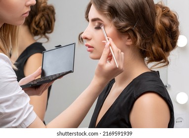 Hairdresser And Make-up Artist Doing Hair And Makeup To A Young Attractive Woman In A Black Dress In A Beauty Salon.