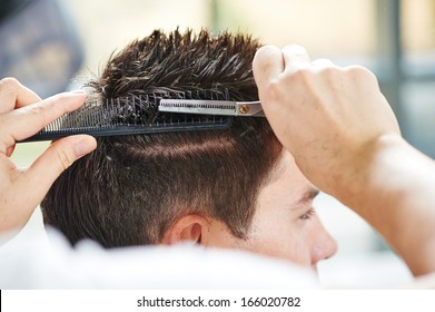 Hairdresser making haircut to young man at beauty parlour