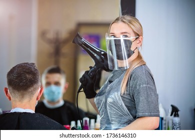 A hairdresser with security measures for Covid-19 holding a hairdryer and looking at the camera in a medicine mask, social distance, cutting hair with a medical mask, eye mask and rubber gloves  - Powered by Shutterstock