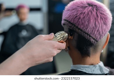 The hairdresser shaves the temple of a female client. Rear view of a woman with short pink hair in a barbershop. - Powered by Shutterstock