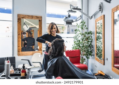 A hairdresser styles a client's hair in a modern salon featuring large mirrors. The setting is stylish and professional. Concept of stylish hair salon. - Powered by Shutterstock