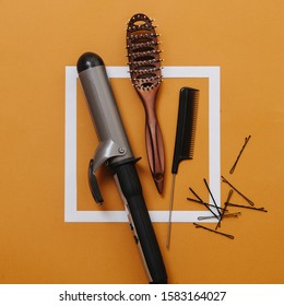 Hairdresser Tools: Curling Iron, Hairbrush, Rat Tail Comb And Bobby Pins. Over Orange Background With White Square On It. Top View. Necessary Things For Styling Hair.