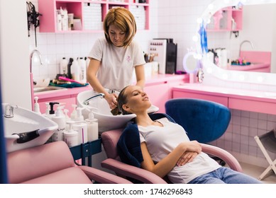 Hairdresser washing hair of woman female customer with a shower at the saloon applying shampoo conditioner on head hair
