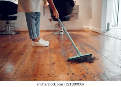 Hairdresser woman, sweeping hair and cleaning salon or barbershop wooden floor after cutting a hairstyle or doing a trim. Feet of female worker with broom for dirt, dust and mess for clean workplace - Powered by Shutterstock