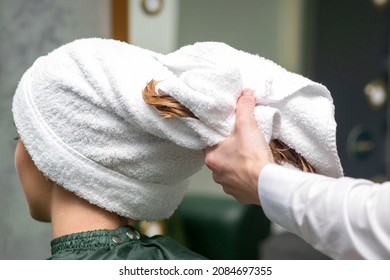 A hairdresser is wrapping the wet hair of the young woman in a towel after washing at the beauty salon - Powered by Shutterstock