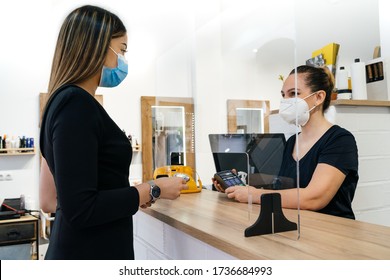 Hairdresser's client paying the hairdresser. They both have a mask on their face due to the coronavirus. They're both very happy - Powered by Shutterstock