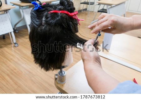 hairdressers cut hair to a mannequin. Mannequinhead is a black long hair.