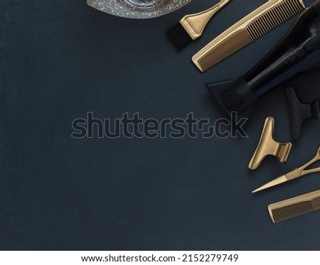 Hairdressing tools in black and gold on gray concrete background. Hair salon accessories, hair dryer, combs, scissors and hair clips in the corner and copy space. 