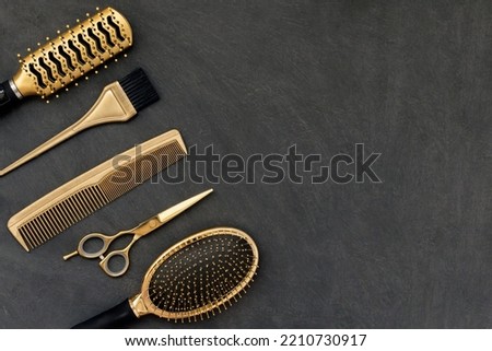 Hairdressing tools in gold on gray concrete background. Hair salon accessories, combs, scissors in the corner and copy space