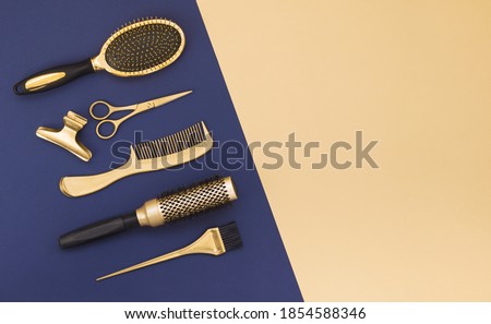 Hairdressing tools on a blue background and a yellow sheet with space for text. Gold hair salon accessories, comb, scissors, hair clip. 
