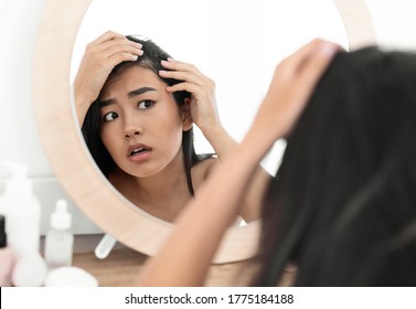 Hairloss Concept. Young Troubled Asian Woman Checking For Thinning Hair In Mirror At Home