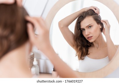 Hairloss Concept. Young Woman Checking For Thinning Hair In Mirror At Home