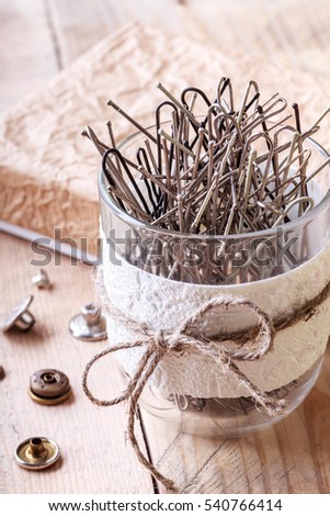 Hairpins in a plastic pot on a wooden background. 
Rivets for jeans on a wooden background. 