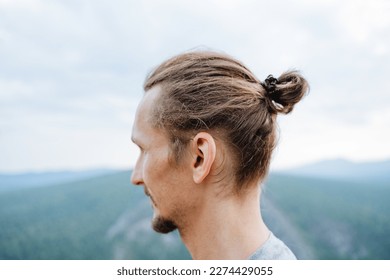 Hairstyle on the head of a man, sloppily collected hair, a view from behind a man's hairstyle, a pigtail on his head, a bearded hipster in the mountains. High quality photo