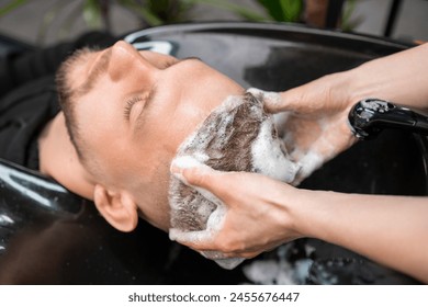 Hairstylist gives relaxing head massage to client washing hair in barbershop. Professional care of customer hairstyle. Spa procedure - Powered by Shutterstock