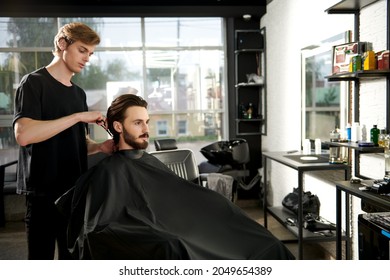 Hairstylist serving a client at a barbershop. Handsome brunet man visiting a hairstylist. Modern hairdressing saloon.  - Shutterstock ID 2049654389