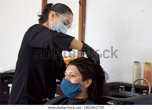 hairstylist wearing\
mask, washing client\'s\
hair