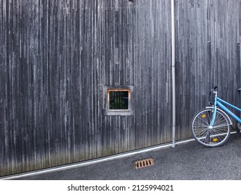 Haldenstein, Switzerland - 05 28 2010: A Blue Bike In Front Of A Wooden Façade With A Small Square Window And A Drainpipe, Along A Steep Road With A Manhole Cover