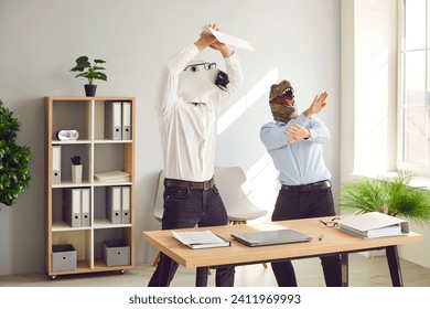 Half animal half people having fun at end of work week. Male corporate workers in horse and dinosaur masks having party. Funny happy men with weird horse and T rex dino faces dancing by desk in office