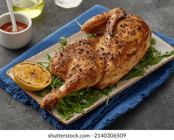 Half Of Appetizing Grilled Juicy Chicken With Golden Brown Crust Served With Lemon Slices, Barbeque Sauce And Papper