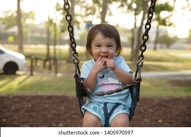 An Half Asian Toddler Is Playing On A Swing In The Park