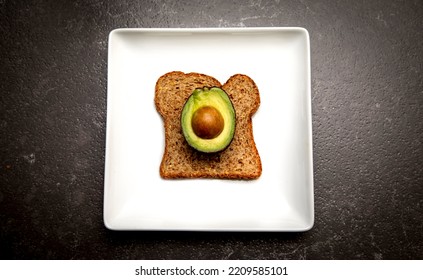 A Half Of An Avacado With A Seed Sitting On A Piece Of Whole Wheat Toast On A White Plate 