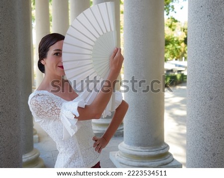 half body flamenco dancer looking at the camera and using an open white fan. dressed in a red pink skirt and red rose