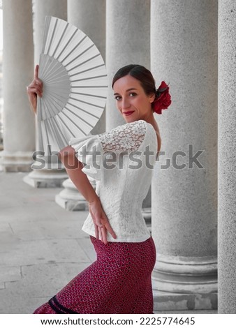 half body flamenco dancer looking at the camera and using an open white fan. dressed in a red pink skirt and red rose