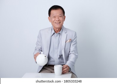 Half body of an happy asian old man in light blue suit and beige pants drinking coffe in studio white background.