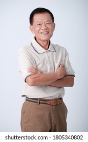 Half Body Of An Happy Asian Old Man In Beige Polo Shirt And Brown Pants Standing And Fold One's Arms Across The Chest  In Studio White Background.