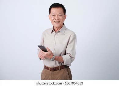 Half body of an happy asian old man in light grey shirt and light brown pants text messaging through cell phone in studio white background.