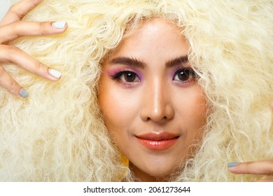 Half Body Portrait Of 20s Asian Caucasian Beautiful Woman Blonde Afro Hair High Fashion Make Up. Cute Girl Smile Look At Camera Over Pastel Red Blue Yellow Colorful Sky Cloud In Studio