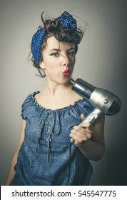 Half Body Portrait Of Housewife In Vintage Clothes Pointing Modern Hair Dryer At Face