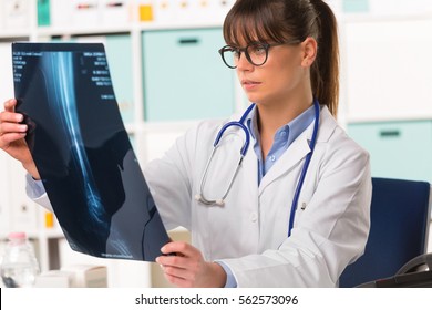 Half body portrait of young female doctor in white coat with stethoscope looking at patients x-ray - Shutterstock ID 562573096