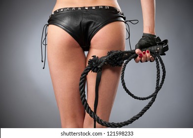 Half body shot of sexy womans buttocks in black underwears on gray background with a whip in his hand