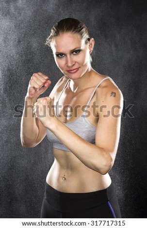 Similar – Close up front portrait of one young athletic woman in sportswear in gym over dark background, standing in boxing stance with hands and fists, looking at camera