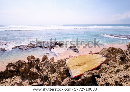 Half of a broken vanilla-red surfboard left behind on a dead rift remains on the beach.