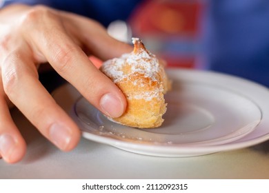 Half a chouquette sprinkled with powdered sugar and held by a man's hand. Colombian bakery food. Colombian repolla