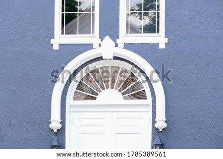 A half circle transom window is under two other windows.  The federalist building is blue with white trim.