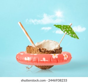 Half of a coconut with ring float, sun umbrella and cocktail straw on a blue background. Creative concept summer beach holiday
