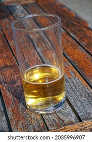 Half Empty Beer In Glass. Half Pint On Wooden Table