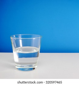 Half Empty Or Half Full Glass Of Water On White Table On Blue Background. (#1)