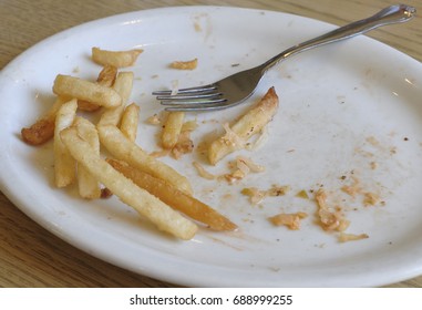 A Half Empty Plate Of Fries On A White Place With A Fork.