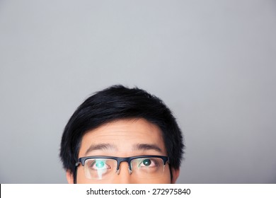 Half Face Portrait Of Asian Man In Glasses Looking Up At Copyspace Over Gray Background