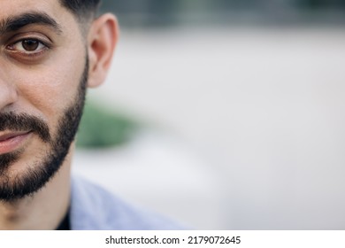 Half Face Of Upset Bearded Caucasian Young Man Looking Straight To Camera While Standing Outdoors In Empty Town. Half Face Portrait Of Young Man With Beard.