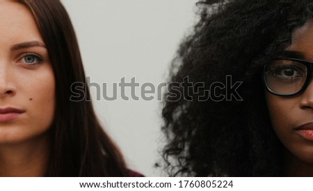 Half faces of two pretty young women on white background. Young attractive couple of multi-ethnic friends looking at camera. Close-up.