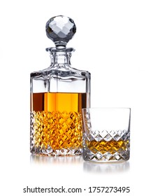 A half full crystal whisky decanter, and crystal glass, with golden whisky, shot on white, with a small reflection