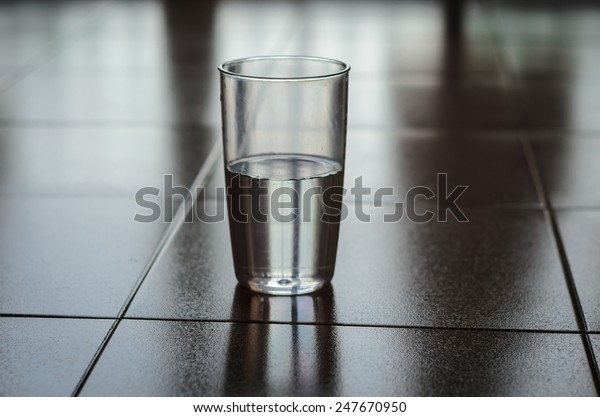 Half Full or Half Empty? Glass\
half filled with plain water put on a floor shot low-key with\
shadow dark background. Reflection of glass is visible on the\
floor.